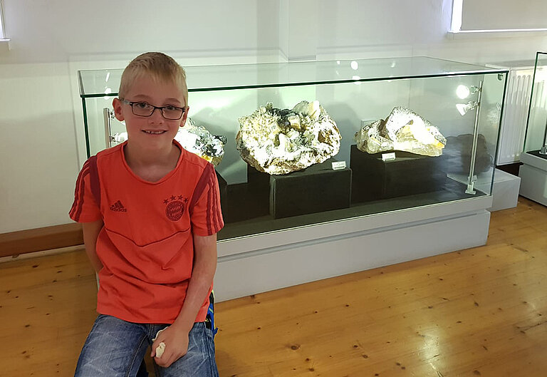 Junge vor Glaskasten mit Mineralgestein